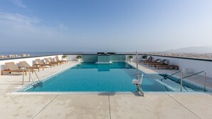 A rooftop infinity pool with lounge chairs and a city view.