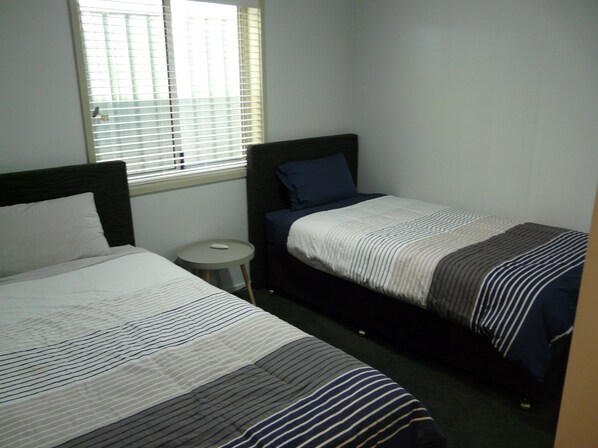 A bedroom with two single beds, a small round table, and a window with blinds. - Home away from Home (Karabar)