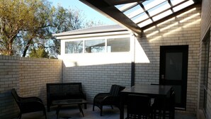 Un patio exterior con una mesa y sillas, un banco y un cerramiento de vidrio con ventana.