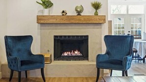Ein Wohnzimmer mit Kamin, zwei blauen Sesseln und einem Holztisch.