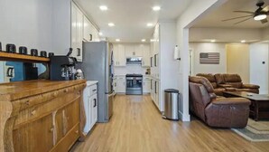 Eine moderne Küche mit weißen Schränken, einer Holz Arbeitsplatte und einem Edelstahl-Kühlschrank. Es gibt eine Sitzecke mit einem braunen Ledersofa und einem Deckenventilator.