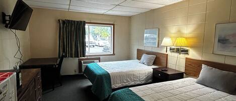 A hotel room with two beds, a desk, a chair, a TV, a window with curtains, a lamp, and a painting on the wall.