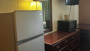 A hotel room with a refrigerator, a wooden dresser, a television mounted on the wall, and a mirror above the dresser. - Grand Inn (Moorhead)