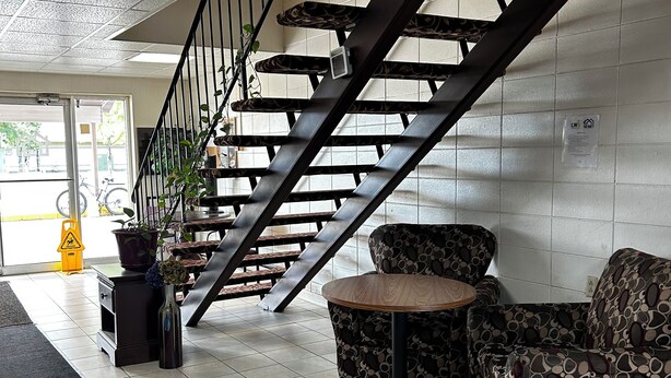 A staircase with a metal railing leading to a higher floor, a potted plant, a patterned sofa, and a small round table. - Grand Inn (Moorhead)