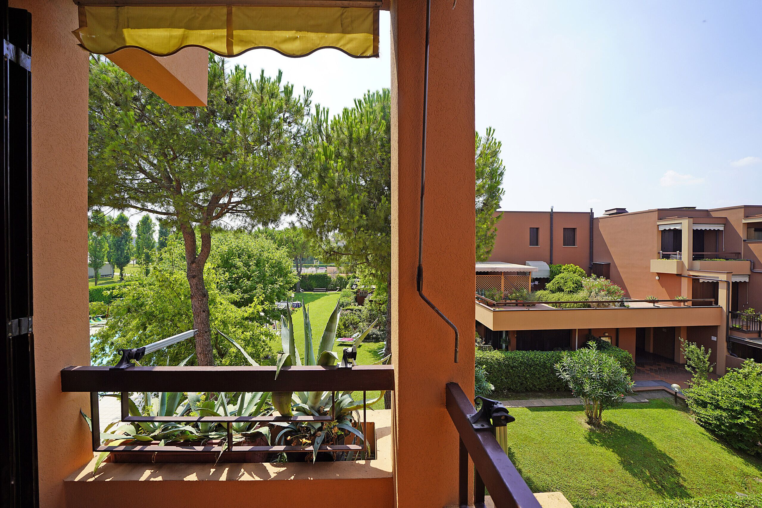 Un balcon donnant sur une cour intérieure, avec des arbres et un bâtiment doté d’un toit plat.