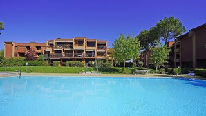 A swimming pool with a clear blue water surface, surrounded by a well-maintained lawn and trees. In the background, there are multi-story buildings with balconies and a flat roof design. - Residence Riviera 43 by Wonderful Italy (Desenzano del Garda)