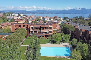 A residential area with a swimming pool, apartment buildings, and a view of a lake and mountains. - Residence Riviera 43 by Wonderful Italy (Desenzano del Garda)