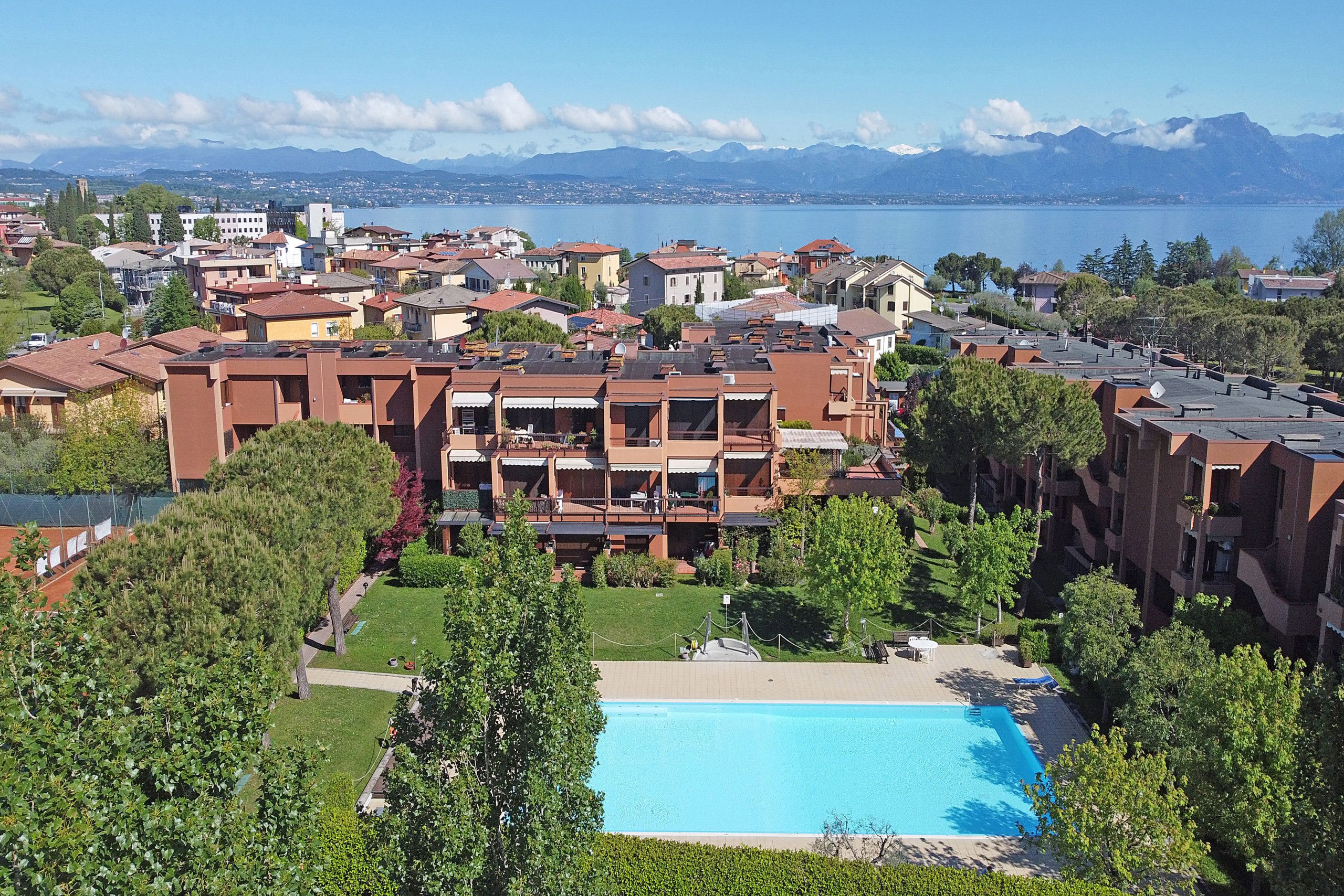 A residential area with a swimming pool, apartment buildings, and a view of a lake and mountains.