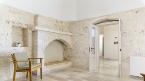Une pièce avec un mur en pierre, une cheminée, une chaise en bois et un sol carrelé.
