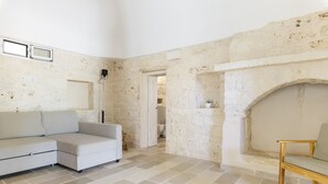 Une pièce avec un mur en pierre, un canapé blanc, une chaise en bois et un sol carrelé.