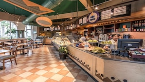 Una cafetería con suelo a cuadros, una barra con vitrina y un panel de menú.