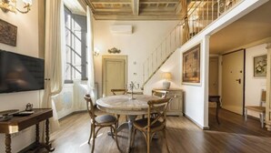 Un espace repas comprenant une table ronde et quatre chaises, un lustre et un escalier menant à un niveau supérieur.