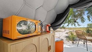 A room with a wooden cabinet, a large orange microwave, and a view of a garden.