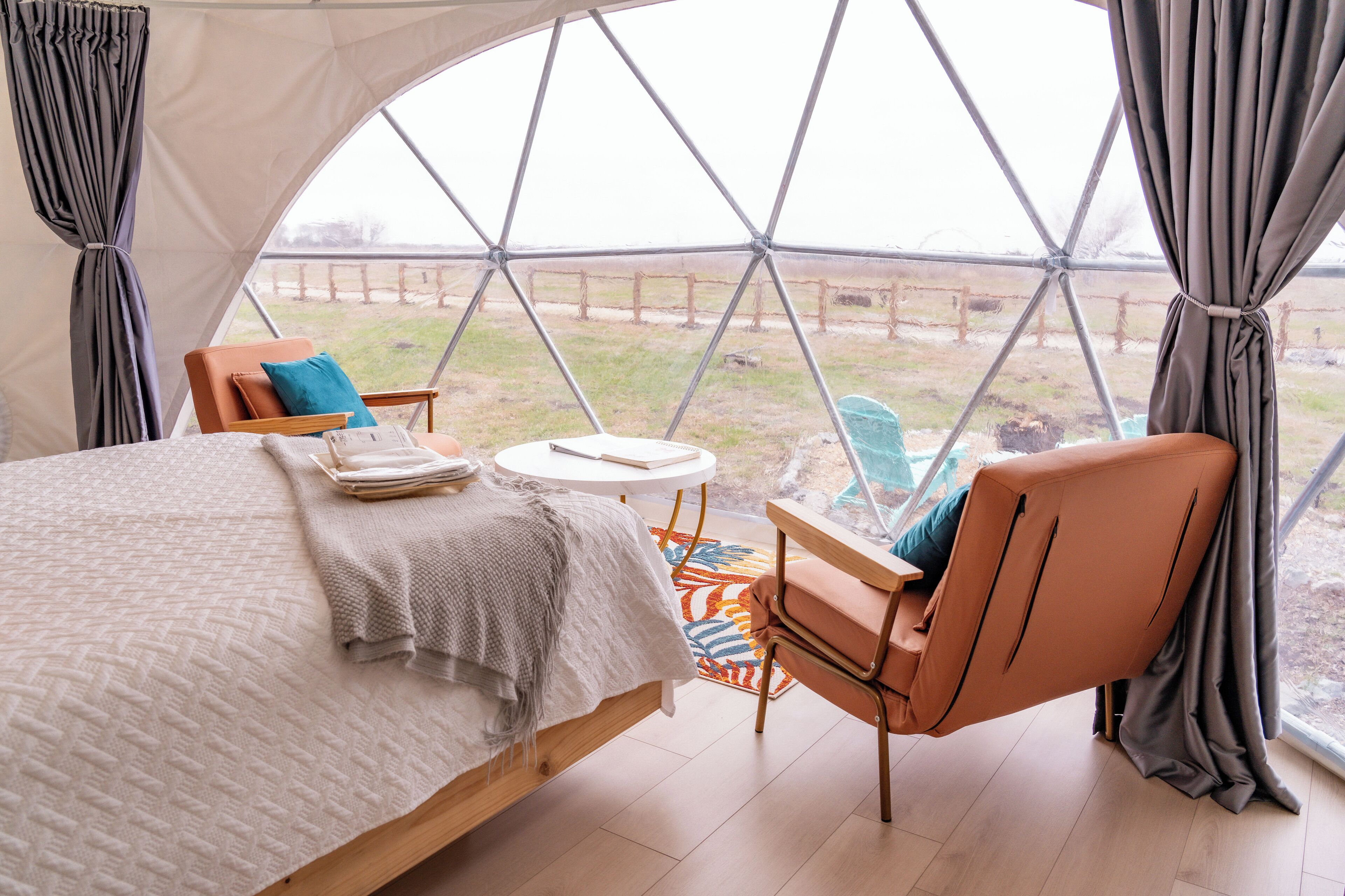 A bedroom with a bed, a chair, a small table, and a view through a large window.