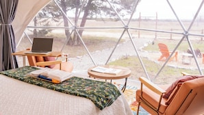 A tented accommodation with a bed, a laptop, a small table, and a view of the outdoors.