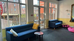 A room with large windows, a blue sofa, a small table, and a pink bean bag. - The Ullswater House  (Bournemouth)