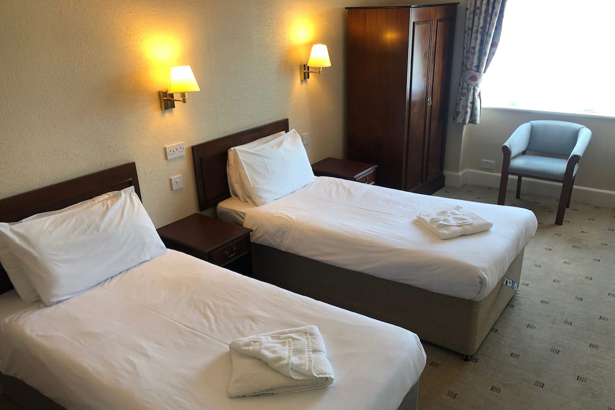 A hotel room with two beds, a nightstand, a wardrobe, a chair, and two wall-mounted lamps.