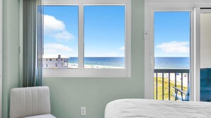 Ein Schlafzimmer mit Blick auf Strand und Meer, ein Stuhl und ein Bett.