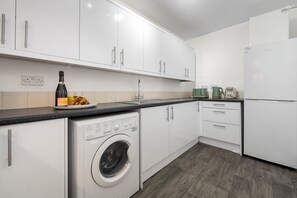 Une cuisine moderne avec des meubles blancs, un lave-linge encastré, une machine à café et une bouteille de champagne.