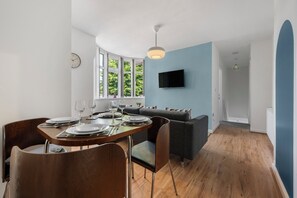 Et moderne spiseområde med et træbord dækket til fire personer, en grå sofa og et tv ophængt på væggen.