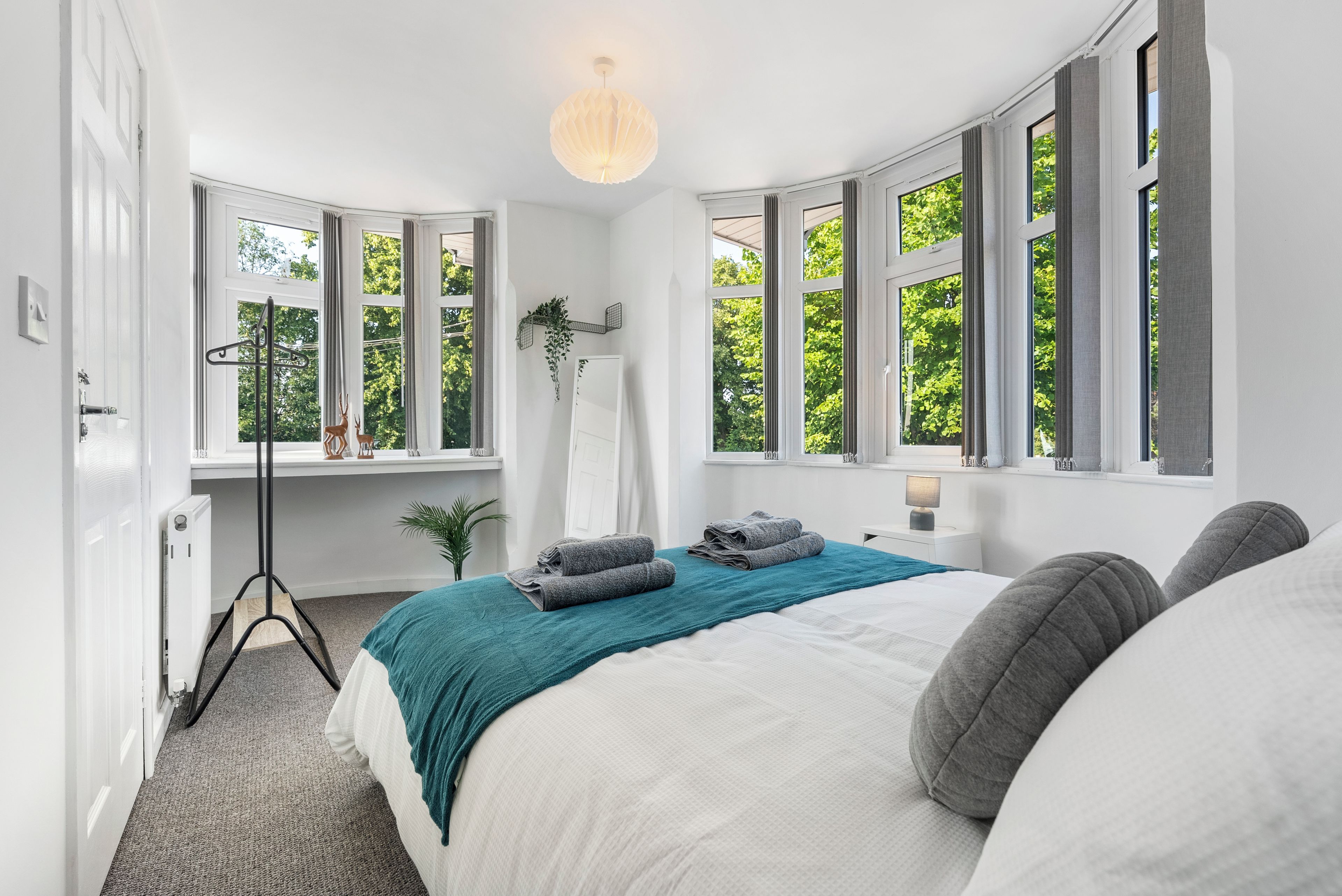 A bedroom with a large bed, a floor lamp, and a window with a view of trees.