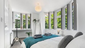 Una camera da letto con un letto grande, una lampada da terra, uno specchio e vista sul verde attraverso ampie finestre.