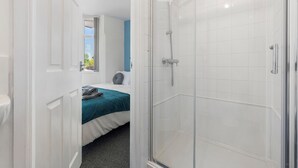 Camera d'albergo con doccia, un letto con copripiumino verde acqua e una finestra vista.