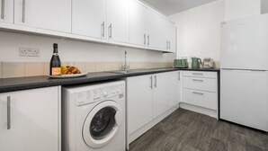 A modern kitchen with white cabinets, a washing machine, a coffee maker, and a kettle. - Modern 4 bed 3 bath apartment, free parking (Coventry)
