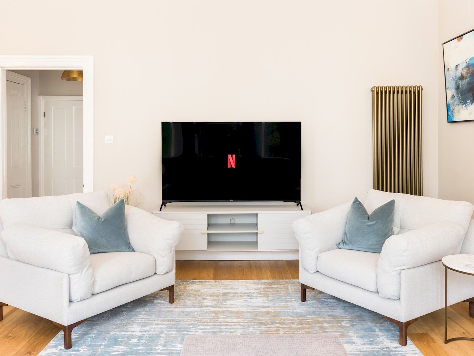 A living room with a flat-screen TV, two white sofas, a small side table, and a patterned rug.