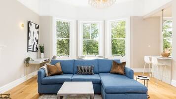 Een moderne woonkamer met een blauwe modulaire bank, een witte salontafel en een kroonluchter.