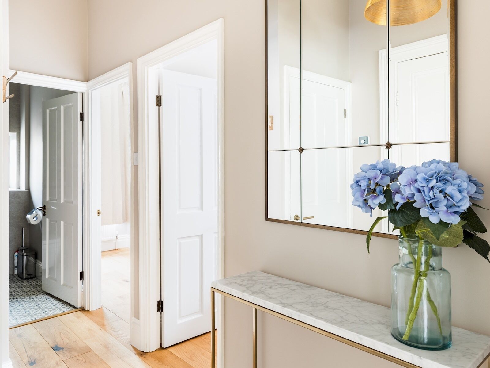 A hallway with a marble-topped console table, a large mirror, and a vase with blue flowers.