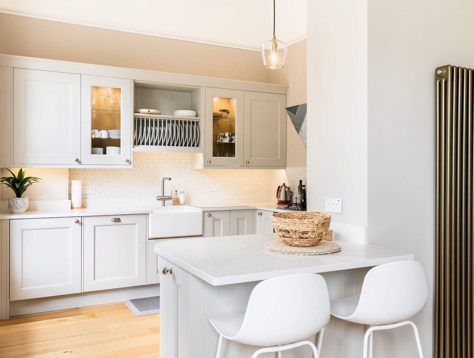 A modern kitchen with white cabinetry, a central island with two chairs, and a hanging light fixture.
