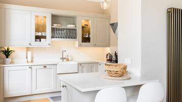 A modern kitchen with white cabinetry, a central island with two chairs, and a hanging light fixture.