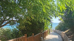 Un sentier pavé de pierres, bordé de rampes en bois, mène à un point de vue panoramique sur la mer.