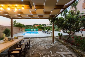 An outdoor pool area with a pergola, lounge chairs, and a dining table with chairs. - Villa Aspa in Prines (Rethymno)