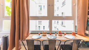 A dining table set with plates, cutlery, and a pitcher of juice, with a window view of buildings and a tree. - WS Jardin du Luxembourg - Boissonade (Paris)