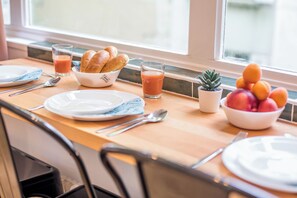 A breakfast table with plates, cutlery, a bowl of bread, a glass of juice, and a bowl of fruit. - WS Jardin du Luxembourg - Boissonade (Paris)