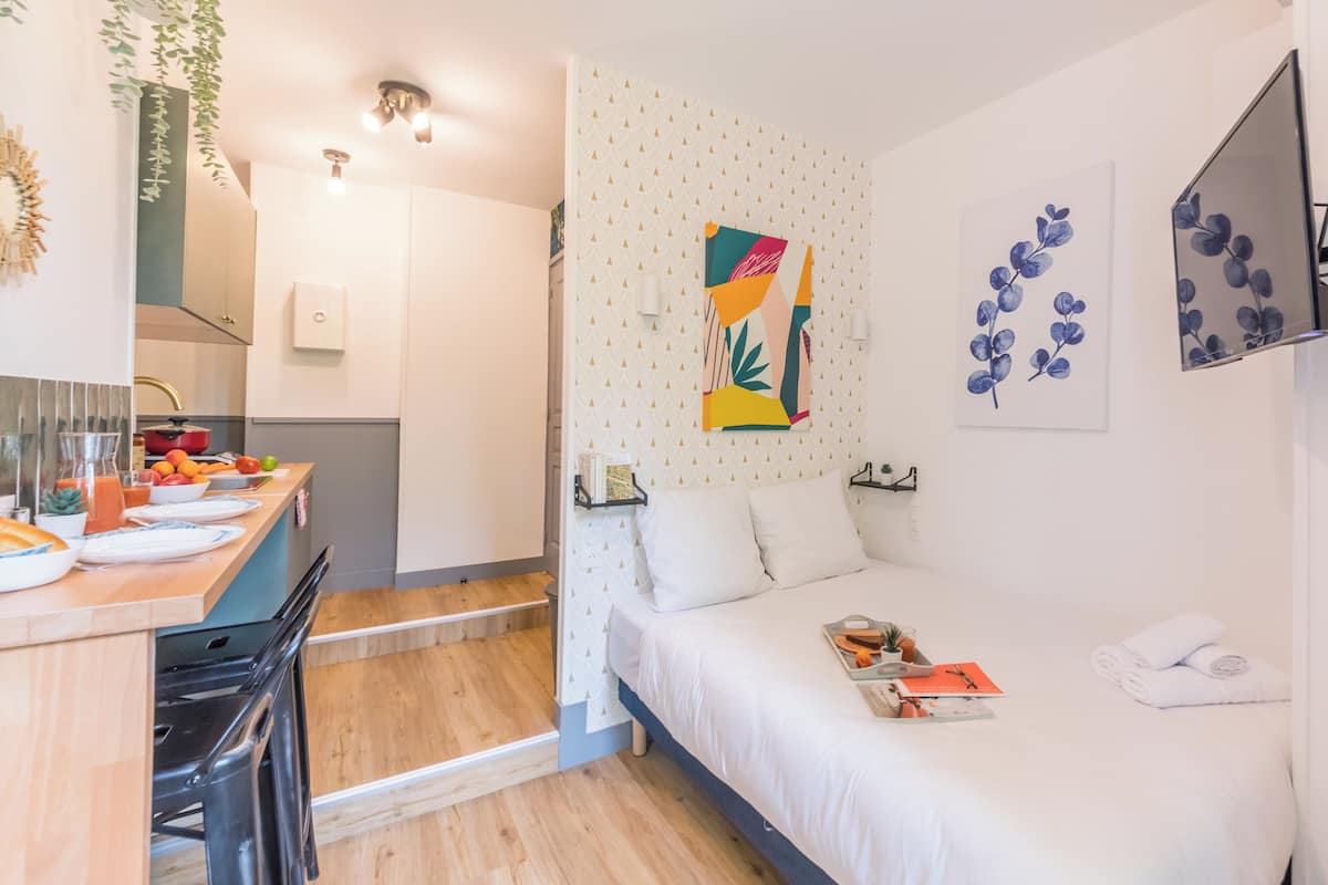 Ein modernes Hotelzimmer mit Bett, kleinem Schreibtisch mit Stuhl, Küchenzeile und Bad.