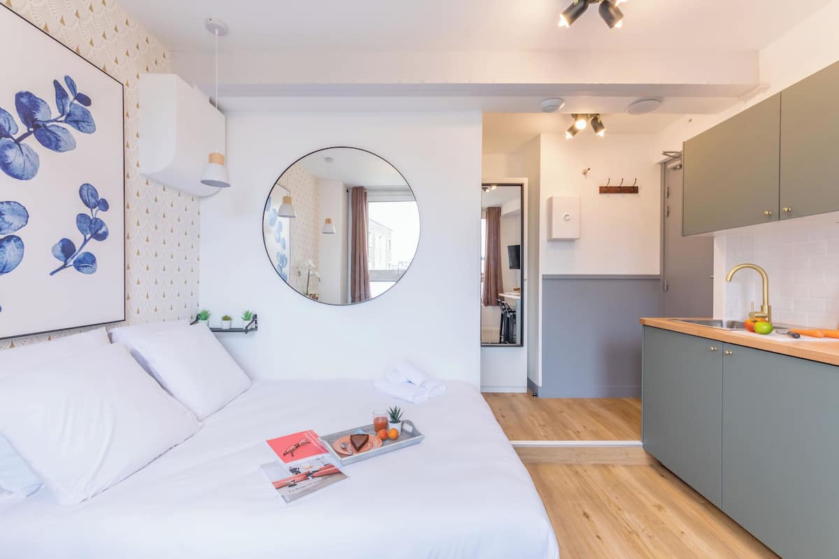 Ein modernes Schlafzimmer mit einem großen Bett, einem Nachttisch mit Frühstücksgedecken, einem Spiegel und Blick in die Küche.