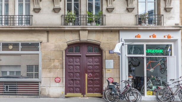 A building with a large, ornate double door and a shop with bicycles displayed outside. - WS Jardin du Luxembourg - Boissonade (Paris)