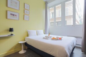 A hotel room with a bed, a bedside table, a lamp, a window with a view of buildings, and a tray with towels and food. - WS Opéra-Folies Bergères (Paris)