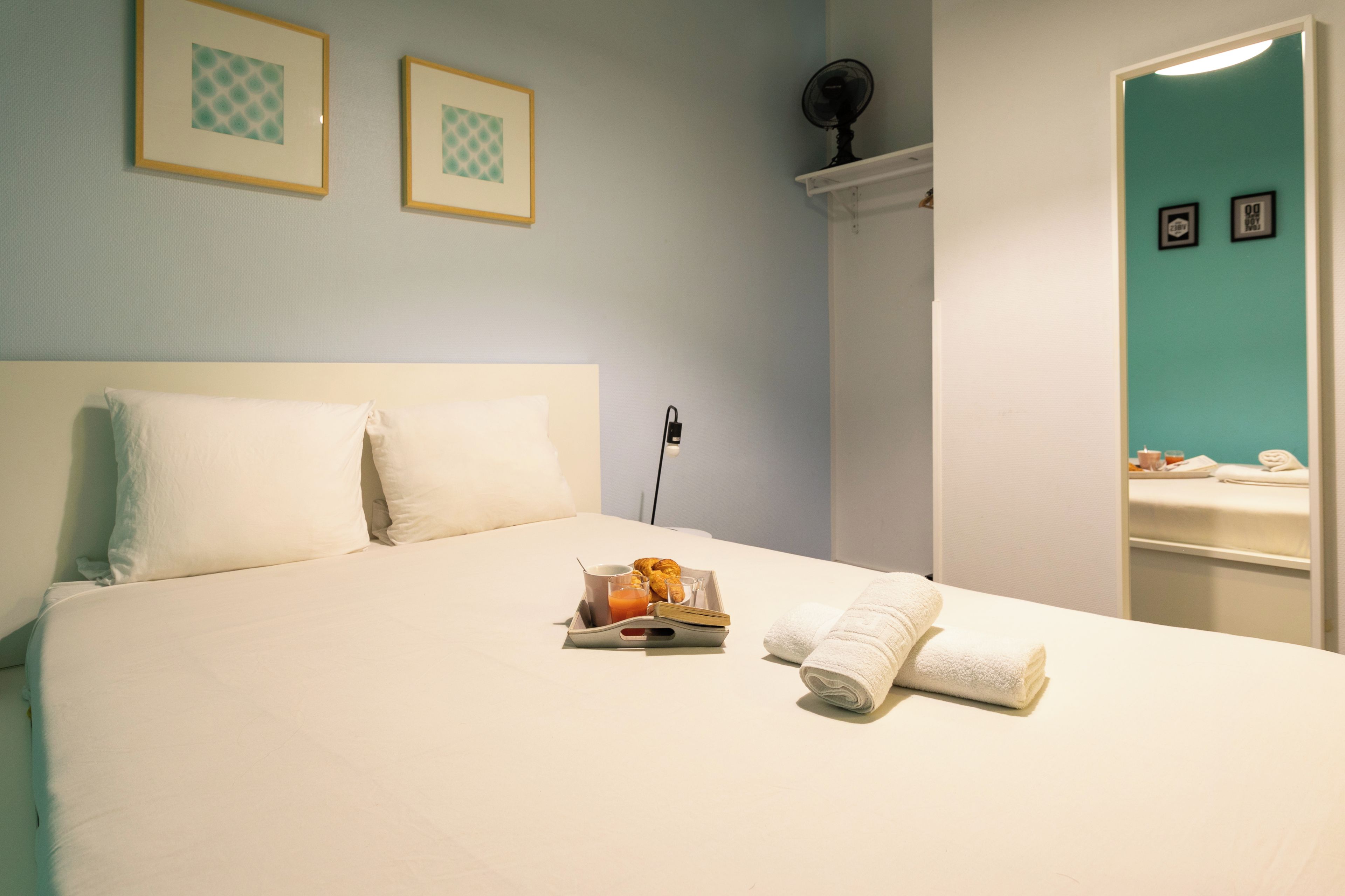 A neatly made bed with white linens, a tray with breakfast items, and two towels.