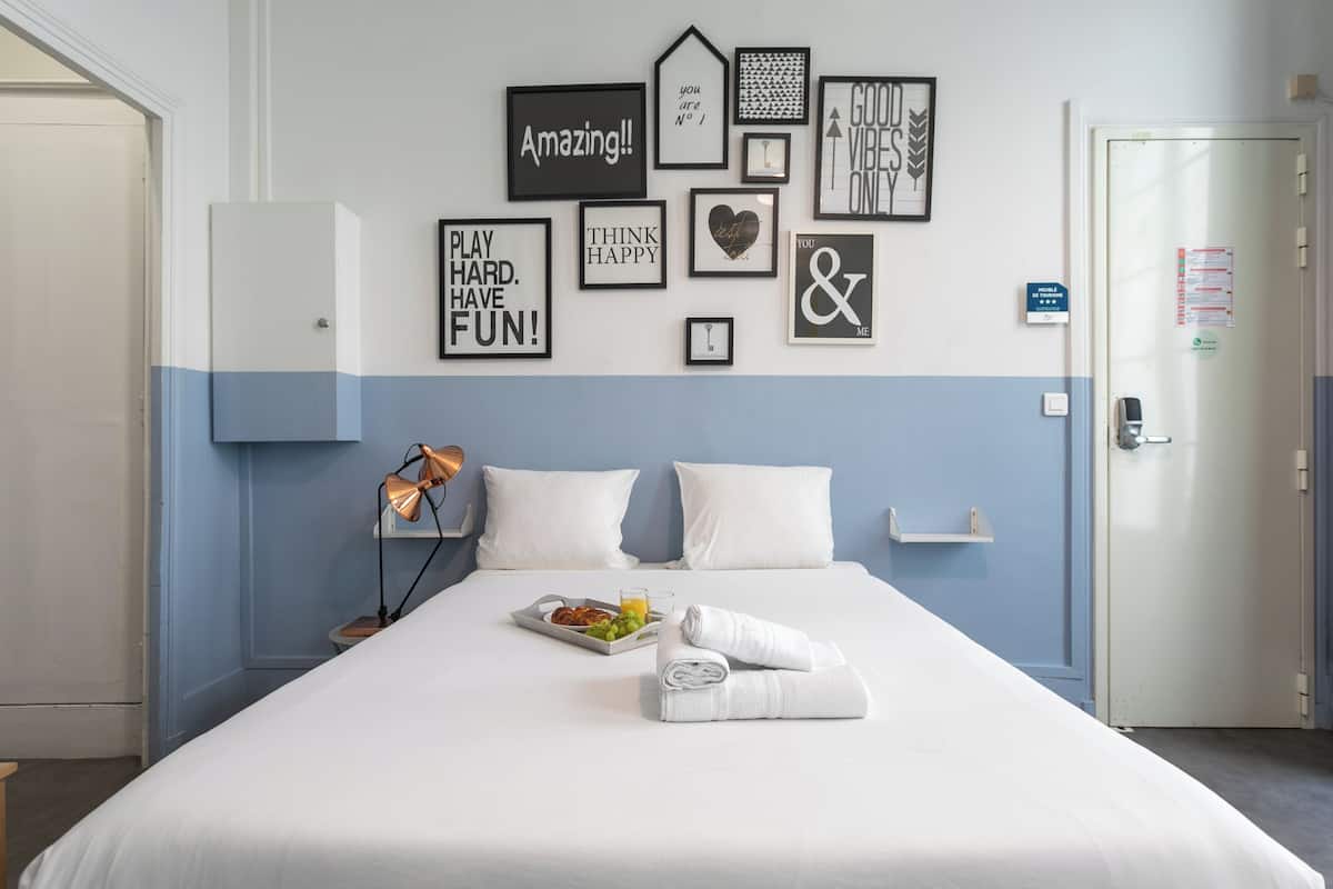 A neatly made bed with a tray of breakfast, a bedside lamp, and motivational wall art in a hotel room.