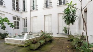 A courtyard with potted plants, a glass-top table, and a white building with windows and doors. - WS Montorgueil-Louvre (Paris)