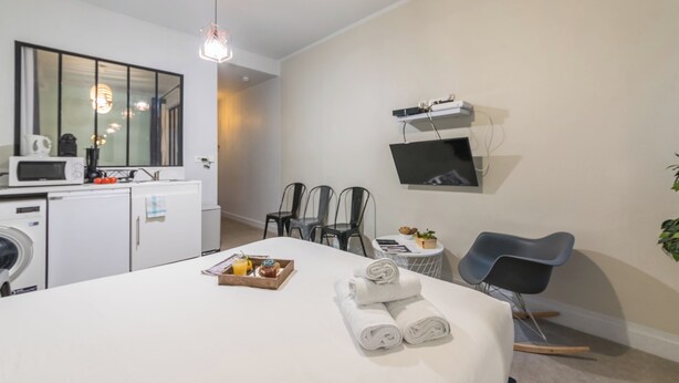 A modern hotel room with a bed, a desk, a microwave, a washing machine, and a TV mounted on the wall. - WS Louvre - Saint Honoré (Paris)