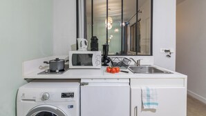 A compact kitchen with a microwave, kettle, sink, and a washing machine. - WS Louvre - Saint Honoré (Paris)