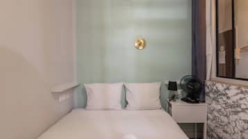 Habitación de hotel con cama, mesita de noche con lámpara y ventilador, espejo y pared con diseño de mármol.