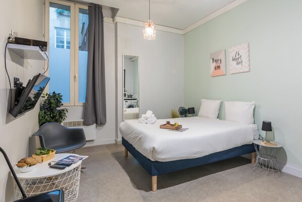 A modern hotel room with a large bed, a desk with a chair, a small table, and a mirror.