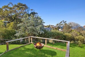 A backyard with a fire pit, wooden deck, and lush greenery.