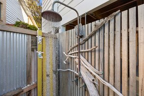 A showerhead with water flowing, a wooden fence, and a corrugated metal wall.